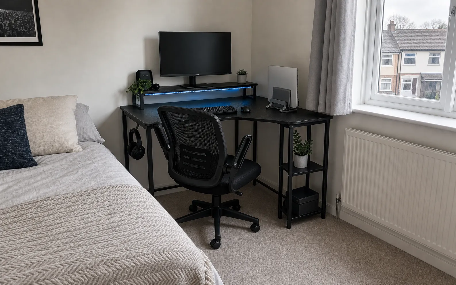 Small corner desk setup in a UK bedroom with a monitor, vertical laptop stand, and compact office chair
